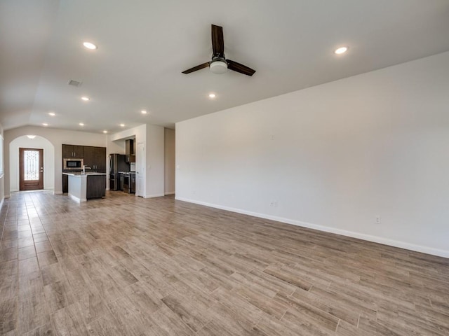 unfurnished living room featuring light wood-type flooring, arched walkways, visible vents, and ceiling fan