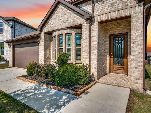 doorway to property featuring a garage, concrete driveway, and brick siding