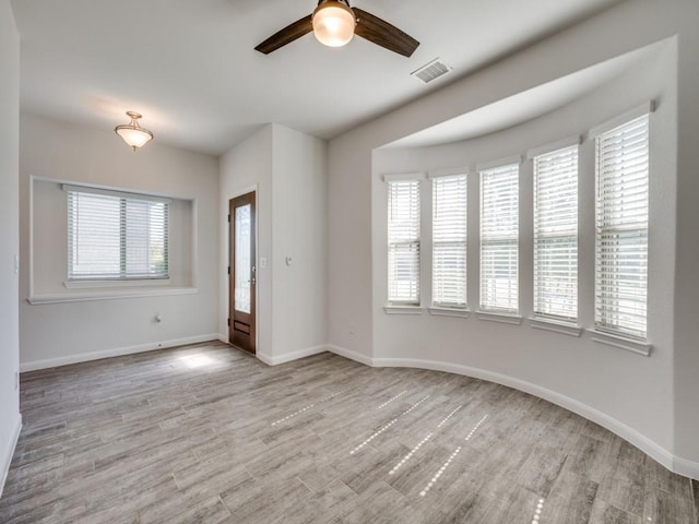 empty room with visible vents, ceiling fan, light wood-type flooring, and baseboards