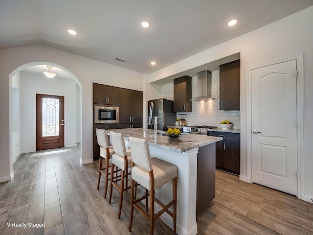 kitchen with visible vents, a breakfast bar, dark brown cabinets, appliances with stainless steel finishes, and wall chimney range hood