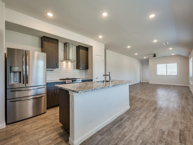 kitchen with light wood finished floors, a sink, decorative backsplash, stainless steel refrigerator with ice dispenser, and wall chimney range hood