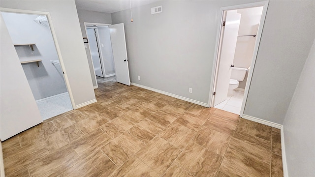 unfurnished bedroom featuring a spacious closet, a closet, and ensuite bath