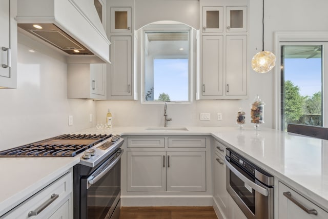 kitchen featuring custom exhaust hood, sink, appliances with stainless steel finishes, decorative light fixtures, and white cabinetry