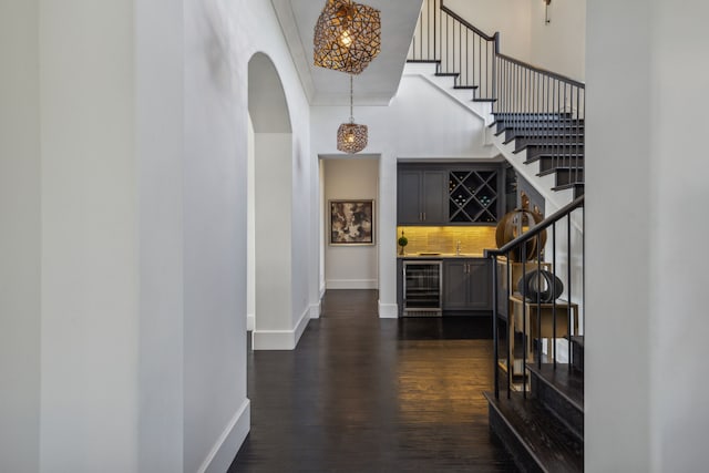 corridor with a high ceiling, beverage cooler, and dark wood-type flooring