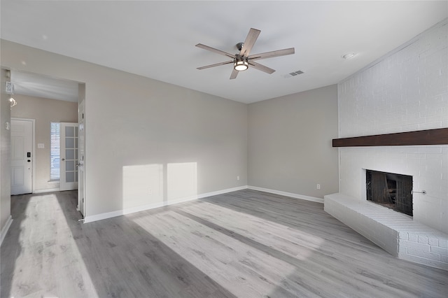 unfurnished living room with a brick fireplace, ceiling fan, and light wood-type flooring