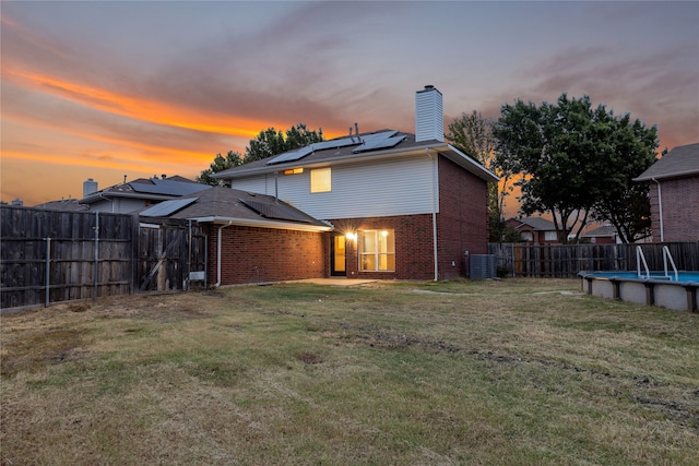 back house at dusk with a fenced in pool, central AC, a lawn, and solar panels