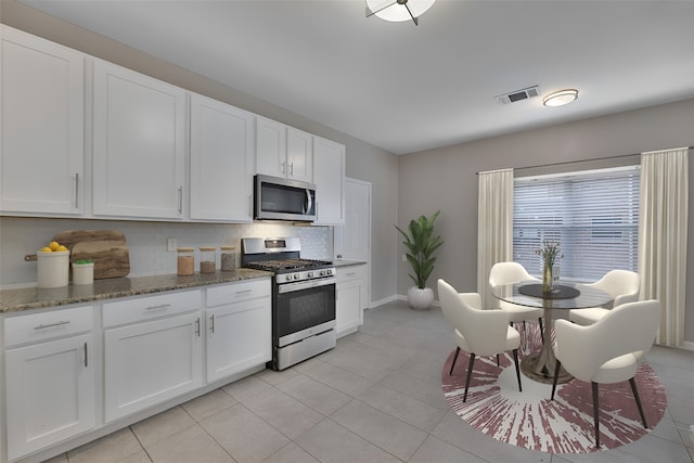 kitchen with decorative backsplash, stainless steel appliances, white cabinetry, and dark stone counters