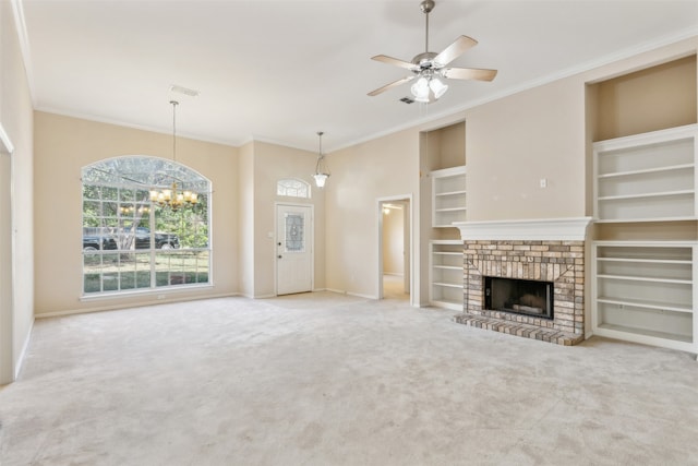 unfurnished living room featuring ceiling fan with notable chandelier, built in features, a brick fireplace, crown molding, and carpet