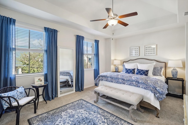 carpeted bedroom with ceiling fan and a raised ceiling