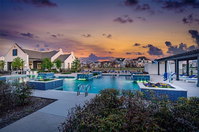 pool at dusk featuring pool water feature, a jacuzzi, a patio area, and a pergola