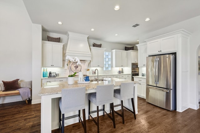 kitchen with custom exhaust hood, a kitchen island with sink, appliances with stainless steel finishes, and white cabinetry