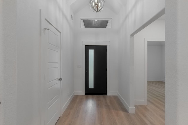 foyer entrance featuring light hardwood / wood-style flooring, an inviting chandelier, and lofted ceiling