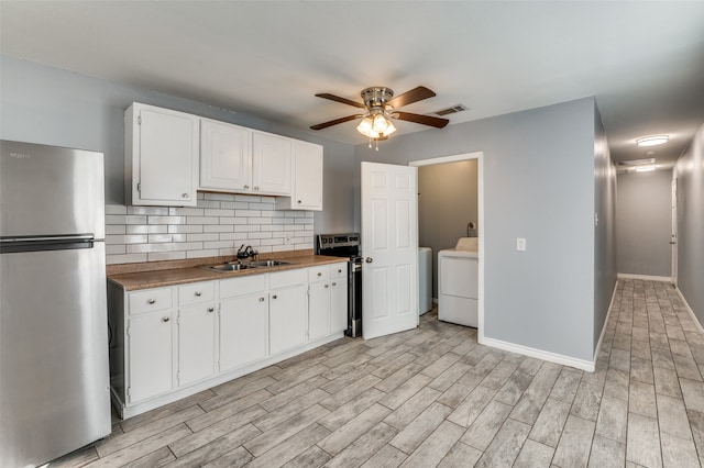 kitchen with washer / dryer, sink, stainless steel fridge, light hardwood / wood-style floors, and white cabinets