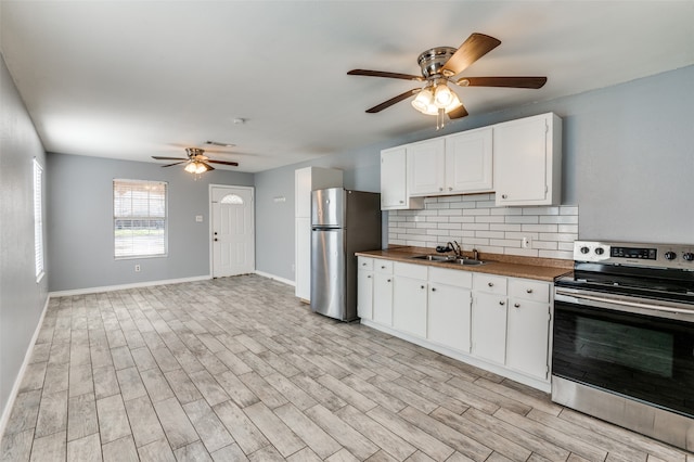 kitchen featuring tasteful backsplash, appliances with stainless steel finishes, white cabinetry, light wood-type flooring, and sink