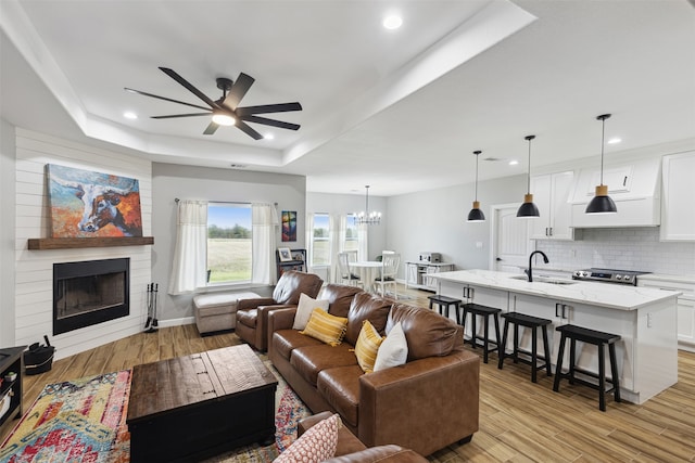 living room with ceiling fan with notable chandelier, a fireplace, light hardwood / wood-style floors, and a raised ceiling