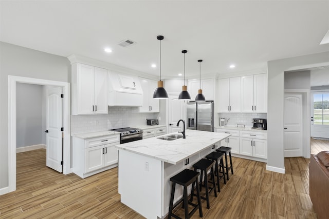 kitchen with white cabinets, stainless steel appliances, a center island with sink, and light wood-type flooring