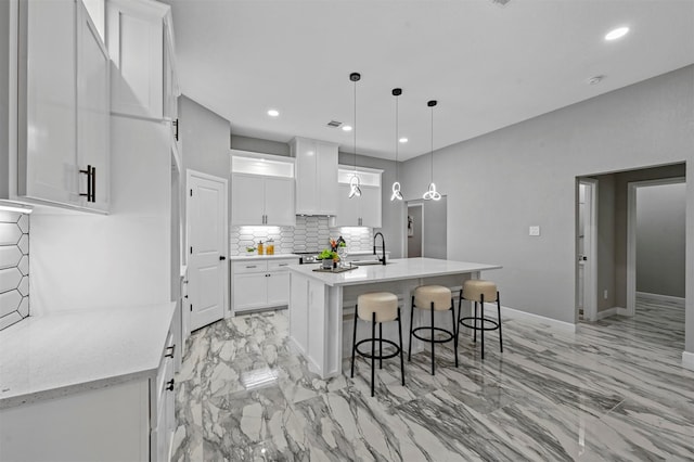 kitchen with sink, white cabinetry, hanging light fixtures, and a kitchen island with sink