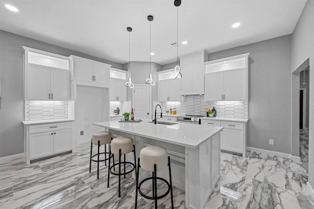 kitchen with a center island with sink, sink, white cabinetry, and pendant lighting