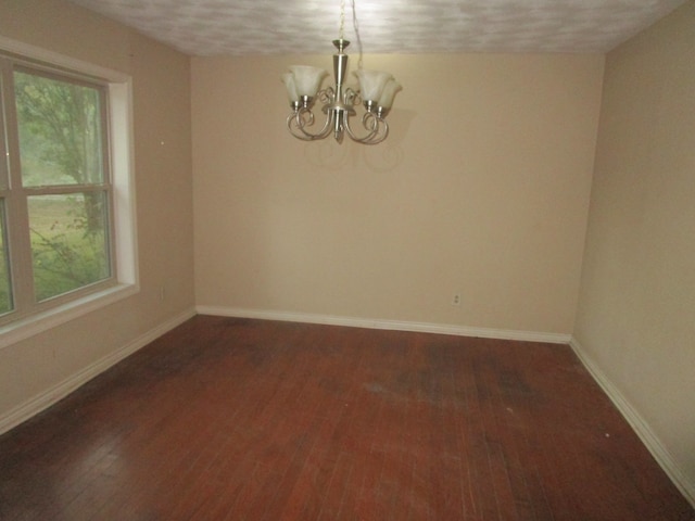 empty room with dark wood-type flooring, a textured ceiling, and a chandelier