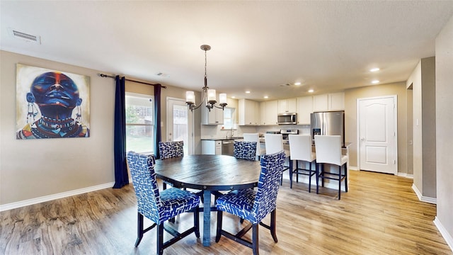 dining area featuring an inviting chandelier, sink, and light hardwood / wood-style floors