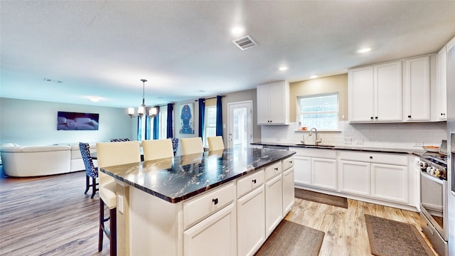 kitchen with sink, a kitchen island, hanging light fixtures, light hardwood / wood-style floors, and a breakfast bar area