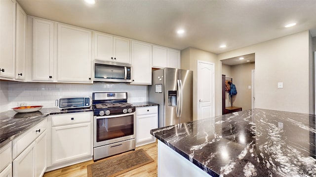 kitchen with white cabinetry, stainless steel appliances, and dark stone counters