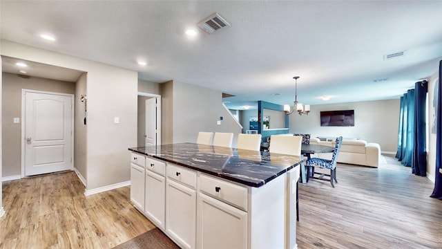 kitchen with light wood-type flooring, a kitchen island, hanging light fixtures, white cabinetry, and a notable chandelier