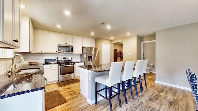 kitchen with a kitchen island, sink, white cabinets, light wood-type flooring, and appliances with stainless steel finishes