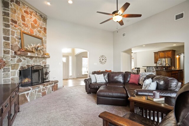 living room with light carpet, a stone fireplace, ceiling fan, and a high ceiling