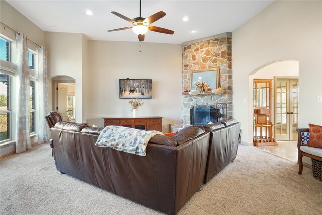 living room with a high ceiling, a stone fireplace, light carpet, and ceiling fan