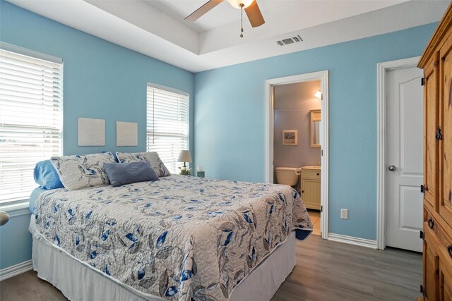 bedroom with a raised ceiling, ceiling fan, dark wood-type flooring, and ensuite bath