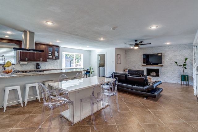 kitchen with tile patterned floors, island exhaust hood, stainless steel gas cooktop, a kitchen breakfast bar, and a fireplace