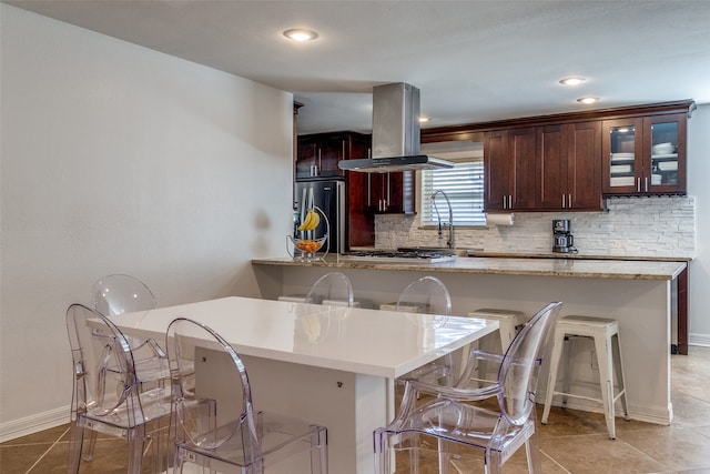 kitchen with island range hood, stainless steel appliances, a breakfast bar, light tile patterned floors, and tasteful backsplash