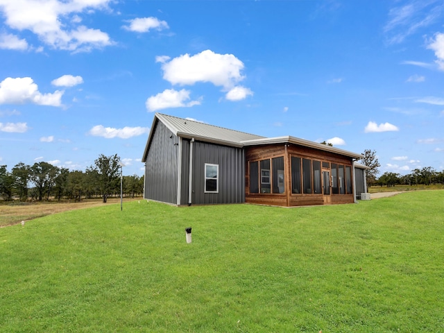 back of property featuring metal roof, a lawn, and a sunroom