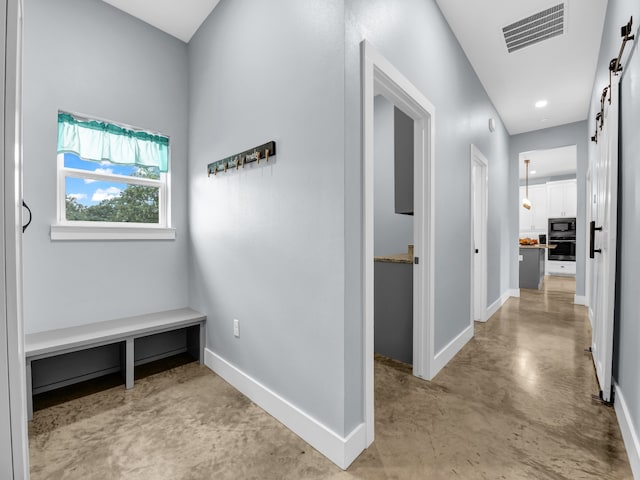 hall with a barn door, concrete floors, visible vents, and baseboards