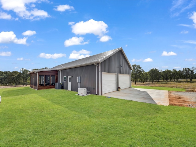 exterior space with a detached garage, concrete driveway, a lawn, a sunroom, and metal roof