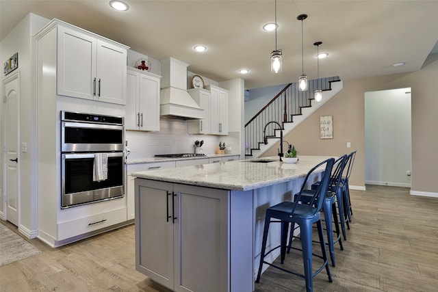 kitchen featuring white cabinets, custom range hood, sink, and a center island with sink