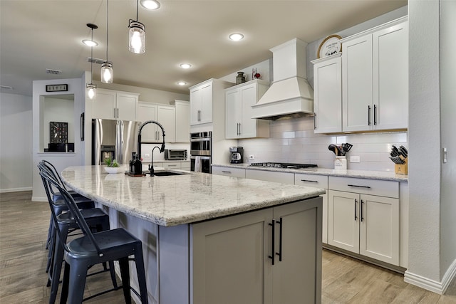 kitchen with white cabinets, a kitchen island with sink, stainless steel appliances, and custom range hood