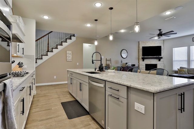 kitchen featuring an island with sink, sink, decorative light fixtures, white cabinetry, and a fireplace