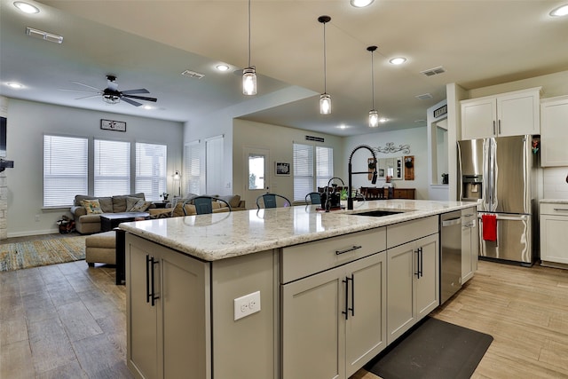 kitchen with a center island with sink, light stone countertops, light hardwood / wood-style flooring, sink, and stainless steel appliances