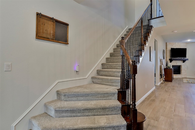 stairs with a stone fireplace and hardwood / wood-style flooring