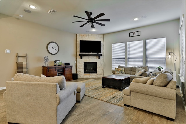 living room featuring a stone fireplace, light wood-type flooring, and ceiling fan