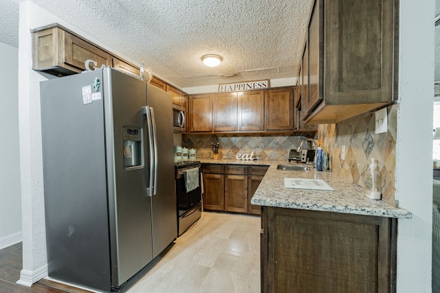 kitchen featuring sink, backsplash, a textured ceiling, stainless steel appliances, and light stone counters