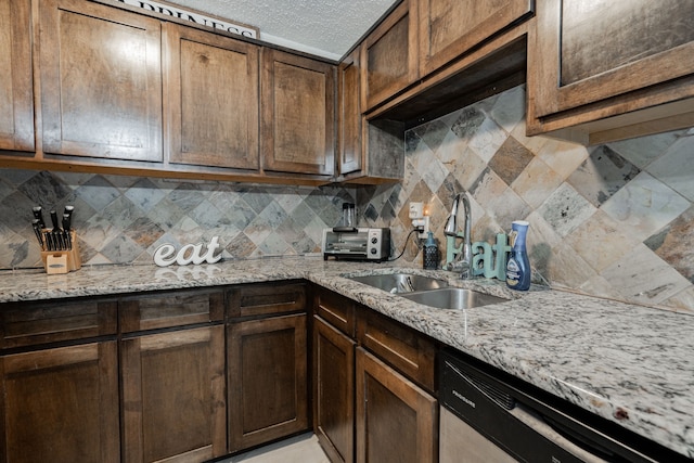 kitchen featuring decorative backsplash, light stone counters, a textured ceiling, stainless steel dishwasher, and sink