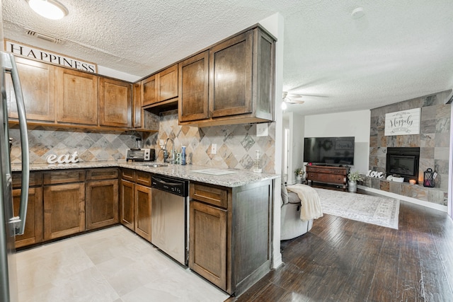 kitchen featuring dishwasher, a textured ceiling, a tile fireplace, light hardwood / wood-style floors, and light stone counters