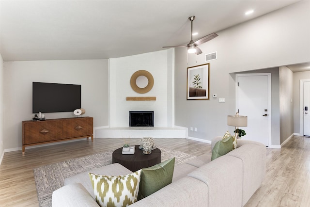 living room featuring a large fireplace, light wood-style flooring, visible vents, and baseboards