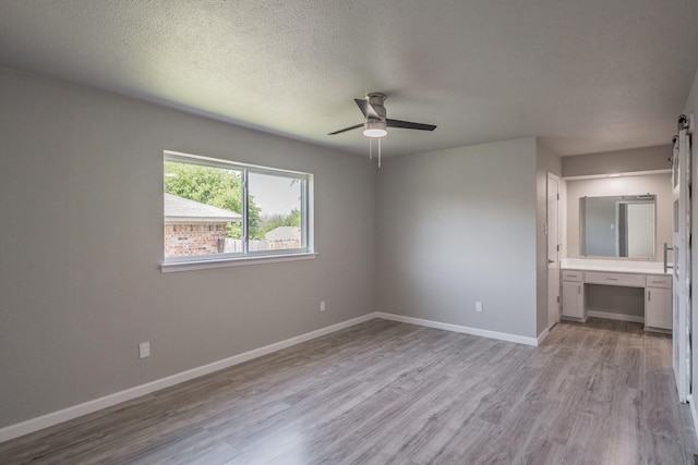 unfurnished bedroom with a textured ceiling, ensuite bathroom, light wood-type flooring, and ceiling fan