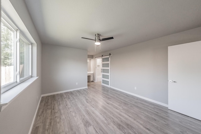 unfurnished bedroom featuring ceiling fan, a textured ceiling, a barn door, light hardwood / wood-style floors, and ensuite bath