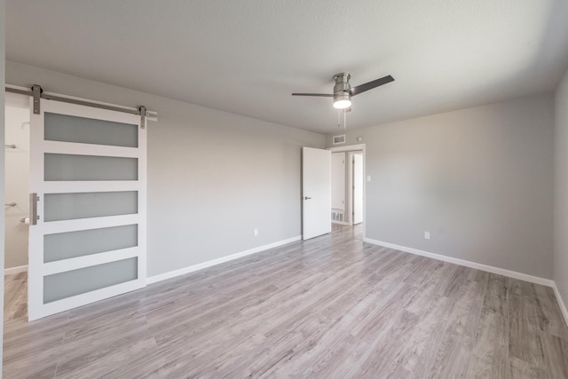 empty room featuring ceiling fan, light hardwood / wood-style flooring, a barn door, and built in shelves