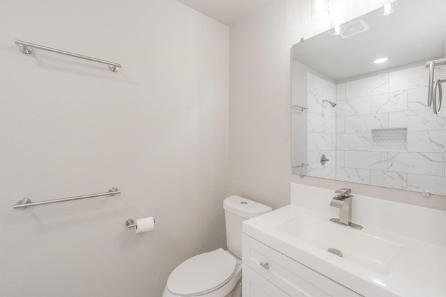 bathroom with a tile shower, toilet, and vanity